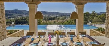 Look from laid dining table of the porch of villa Blakstad in Ibiza to shiny pool and landscape