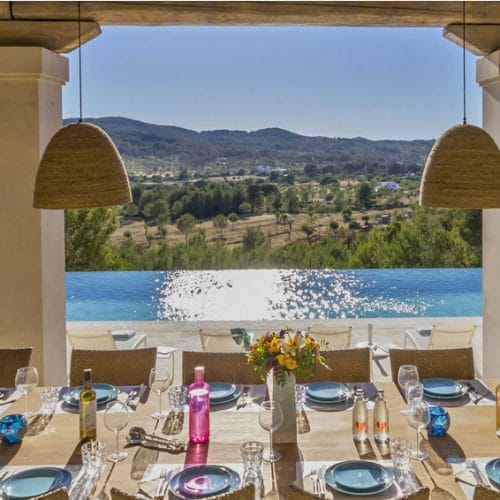 Look from laid dining table of the porch of villa Blakstad in Ibiza to shiny pool and landscape