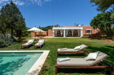 Front view of rustic finca with its garden and pool with loungers