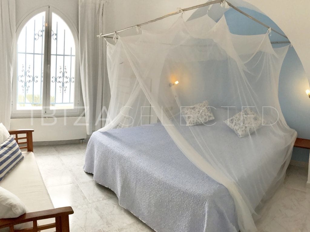 Bedroom with double bed surrounded by mosquito net and arced window