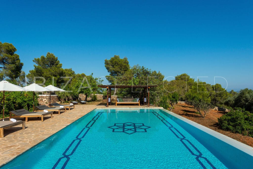 Pool surrounded by sun beds and parasols, a roofed chill-out zone and garden with trees