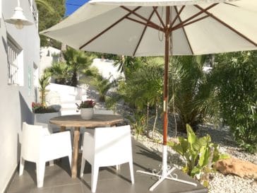 Parasol shaded little table with chairs beside house and garden