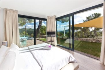 Double bedroom with glass walls open to green lawn garden