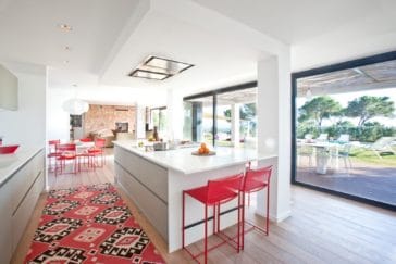 Modern kitchen in white-red design with kitchen centre parallel to veranda's dining area
