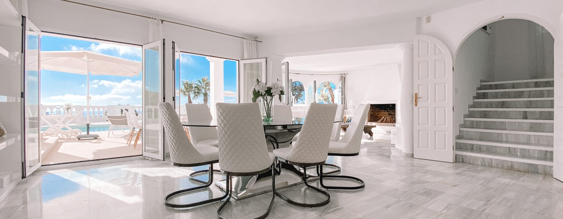 Round glass dining table with white chairs in the living room parallel to pool terrace