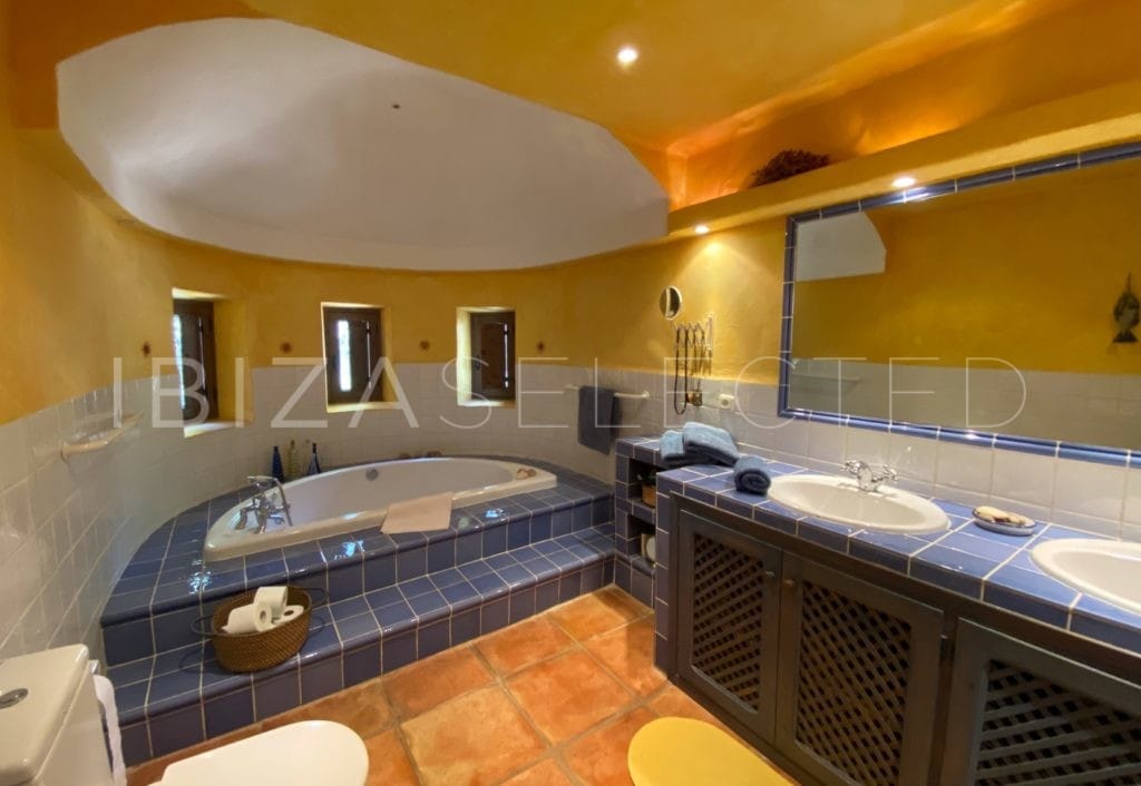 Bathroom in blue and yellow colours with a semicircle bathtub before round wall with little windows, 2 sinks and toilet