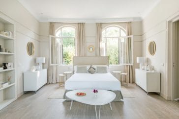 Double bedroom in light beige colours and 2 windows at the head end of the bed