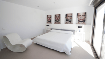 Double bedroom with modern white chair, large windows and pictures of a woman's face on the wall