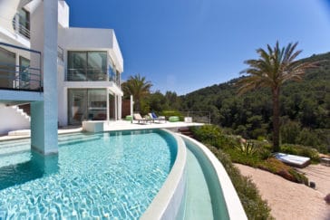 Side front view of luxury villa of 2 floors with glass front walls and round infinity pool overlooking the garden