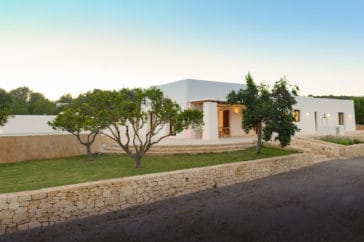 Half front view of house with its veranda and garden with stone wall