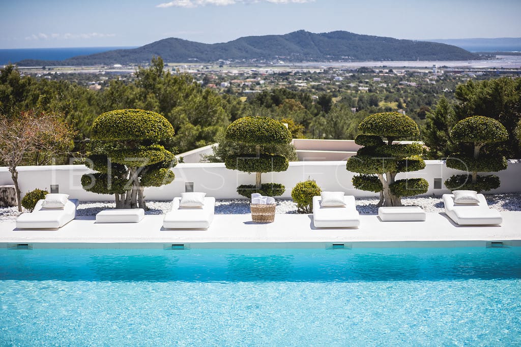 Large pool with comfortable loungers, little pruned trees between them and stunning views over Ibiza town to the sea