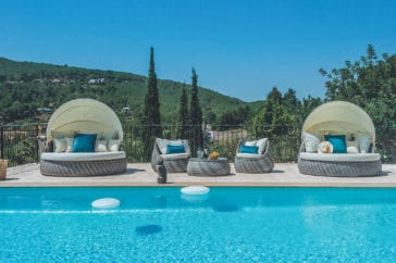 2 parasol covered daybeds and 2 seats with a table in the middle along the pool