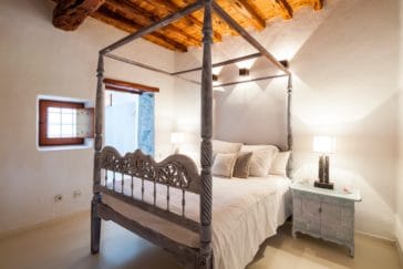 Double bed in room with wooden beam roof and little window