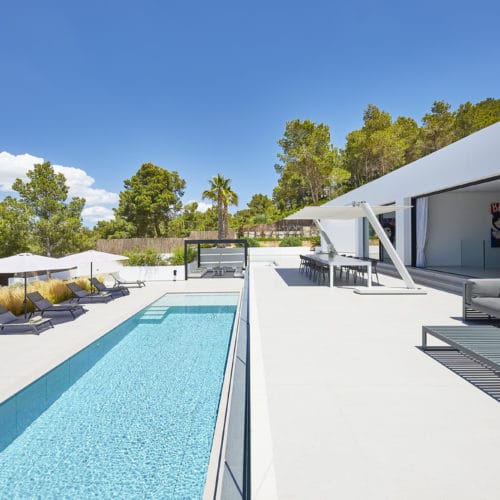 Pool outdoor area with square pool, a modern covered dining area, sun loungers with parasols and a sofa with table
