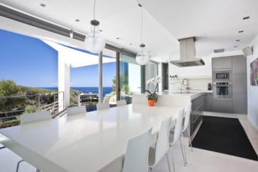 Open kitchen with adjoining white dining table with glass front wall that offers views to the sea