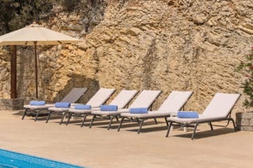 6 sun loungers in front of a stone wall beside a parasol