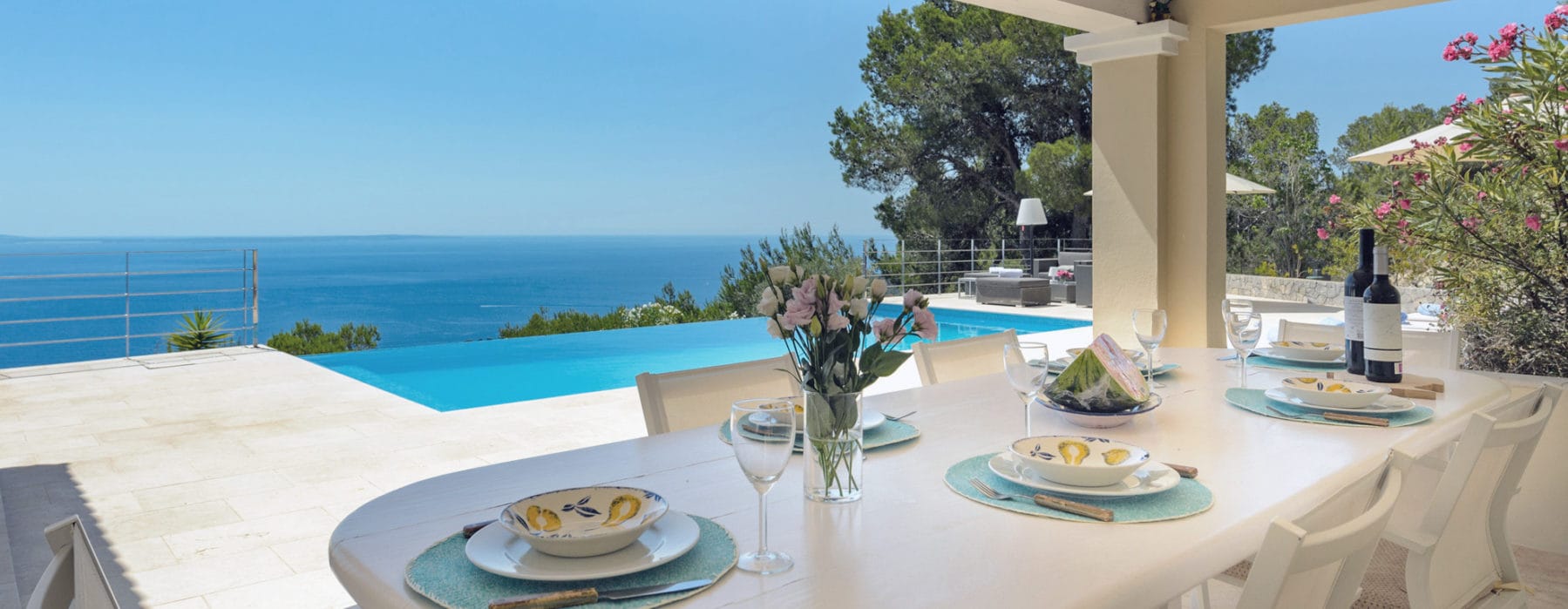 Roofed outdoor dining area with laid white table and white chairs in front of the pool with sea views