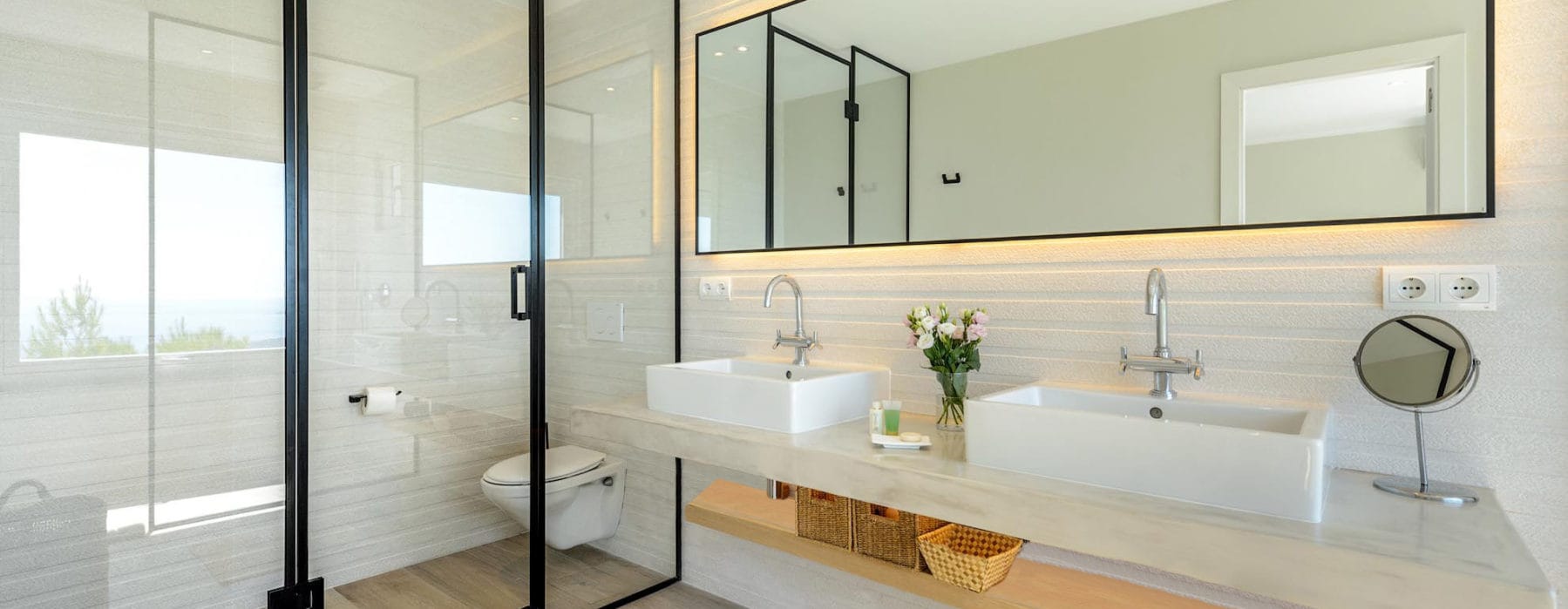 Modern bathroom with 2 sink vanity and through a glass door separated hanging toilet