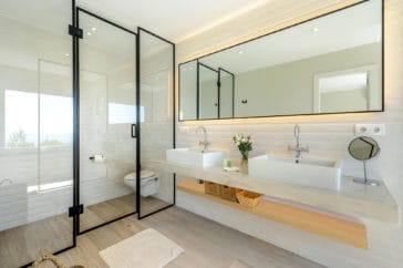Modern bathroom with 2 sink vanity and through a glass door separated hanging toilet