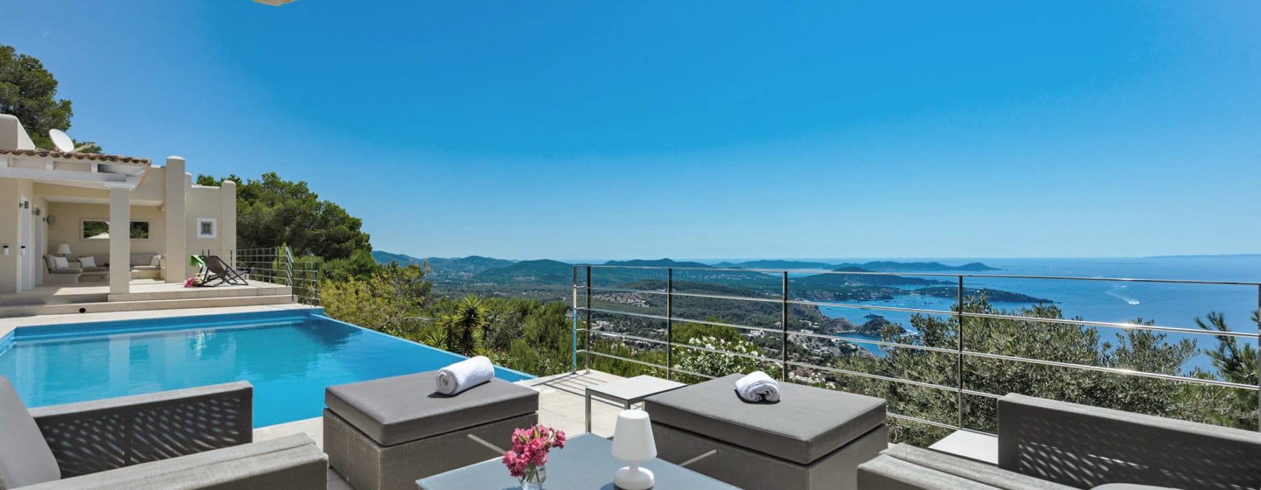 Seating group of 4 comfortable arm chairs, 2 poufs and a low table in between beside the pool with sea views