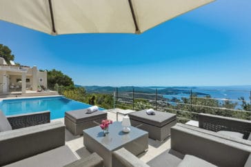 Seating group of 4 comfortable arm chairs, 2 poufs and a low table in between beside the pool with sea views