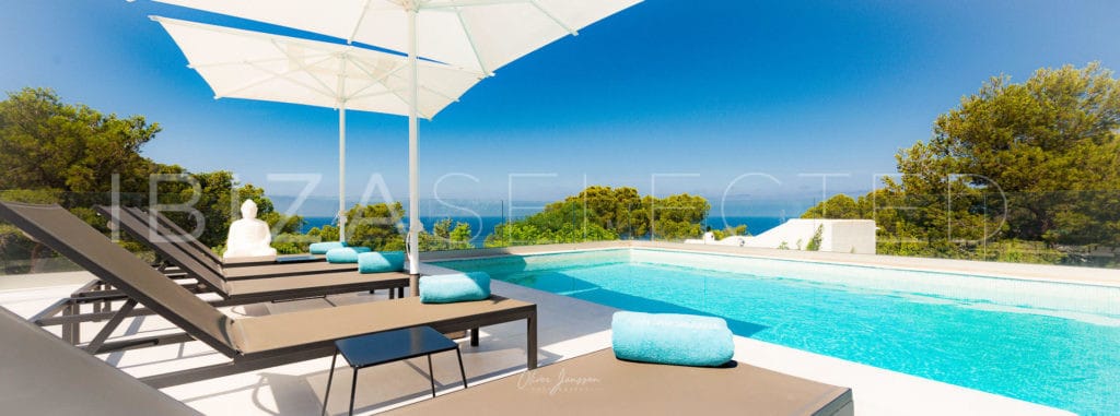 Sun loungers with parasols at the turquoise pool with sea views on the horizon