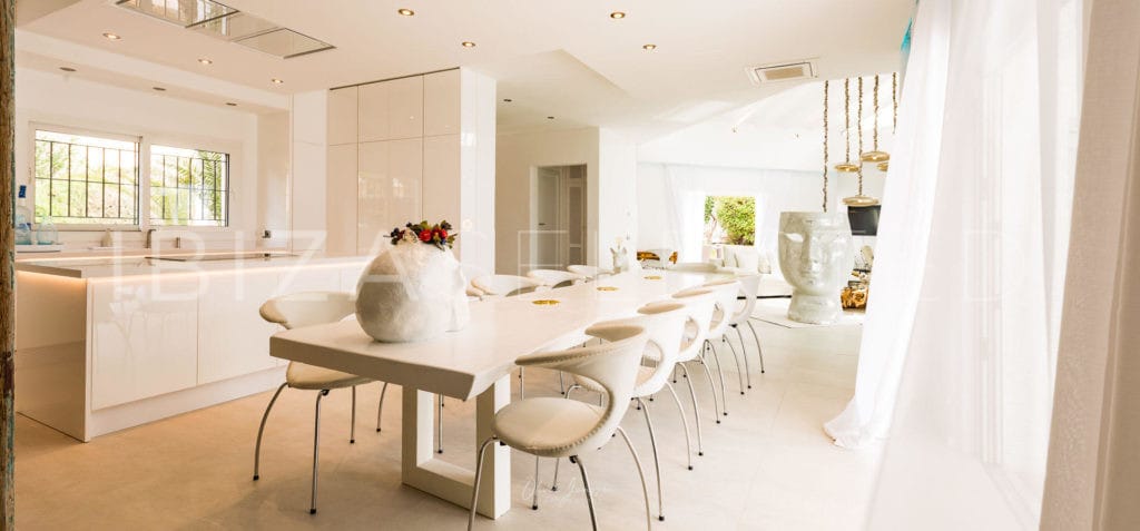 White shiny open modern kitchen with kitchen center beside large light beige dining table