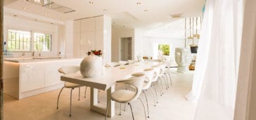 White shiny open modern kitchen with kitchen center beside large light beige dining table