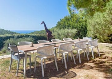 Open air dining table for 10 people in the garden with a giraffe sculpture and sea view