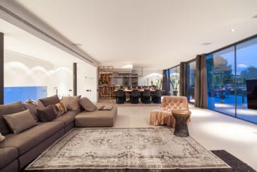 Large sofa with velvet arm chair of open space living room beside dining area and kitchen and glass front leading to terrace