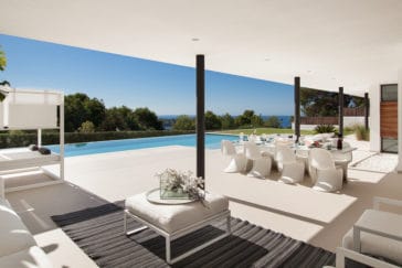 View from roofed veranda with lounge suite and dining table to infinity pool