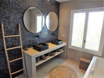 Modern bathroom with 2 sink vanity in front of shiny dark blue colour mosaic wall and bath tub