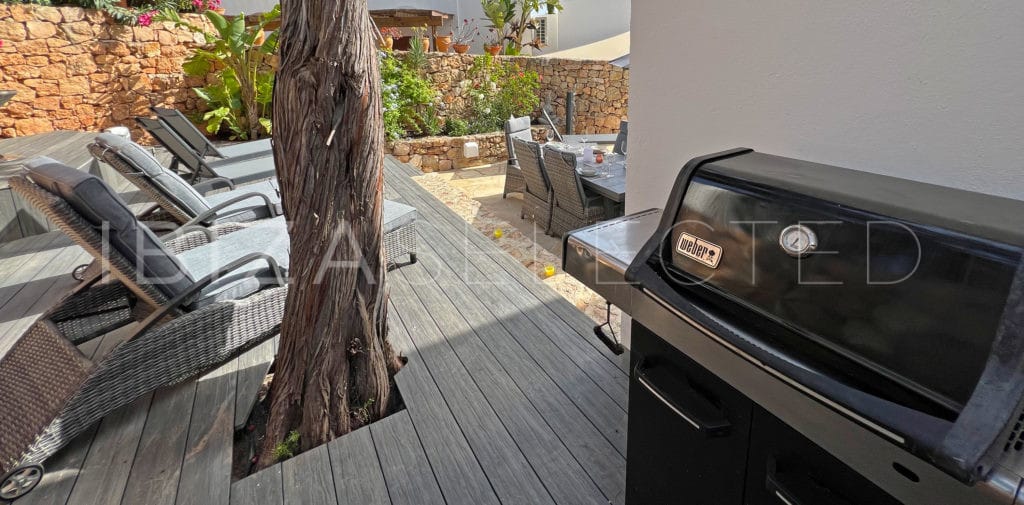 Weber barbecue grill on wooden terrace beside sun loungers und outdoor dining table