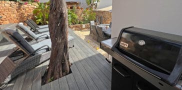 Weber barbecue grill on wooden terrace beside sun loungers und outdoor dining table