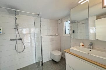 Bathroom with white shiny tiles, walk-in shower, toilet and one sink vanity